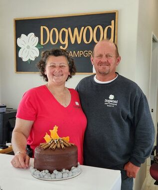 Picture of Lisa & Shawn on opening day with the custom cake our daughter Renee ordered that looks like a campfire.